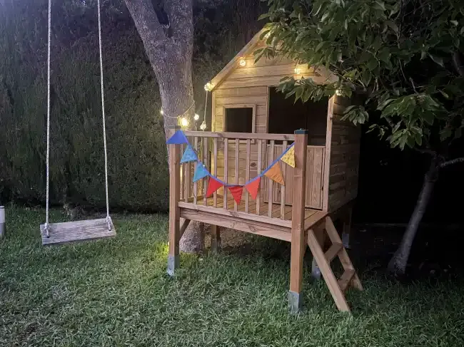 Wooden treehouse and swing in a garden at night